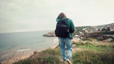 Sırt çantalı ve kameralı bir kadın turistin kışın deniz manzarası ile yol boyunca yürüdüğü yavaş çekimde bir sinema sahnesi..