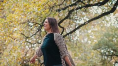 Sinema yavaş çekim görüntüsü. Genç, beyaz bir kadın sonbahar parkında güneşli havanın tadını çıkarıyor..