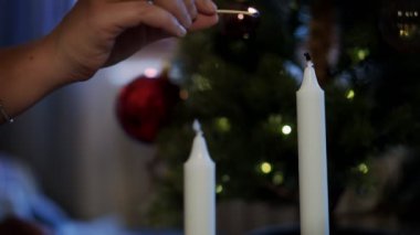 Bir insanın elinin dekore edilmiş bir Noel ağacının arka planıyla bir kibritle mum yaktığı yavaş çekim sineması..