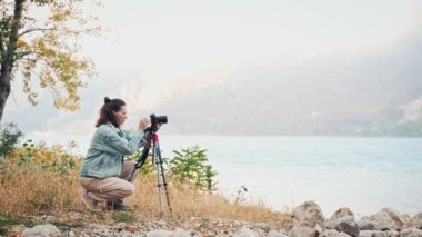 Beyaz kadın profesyonel fotoğrafçı iş başında. Bir tripodun üzerinde kameranın yanında duran ve dağların güzel manzarasının tadını çıkaran bir insan..