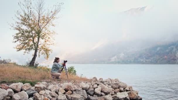 仕事中の若い白人女性プロの写真家 三脚の上にカメラの横に立って 山々の美しい景色を楽しむ人 — ストック動画