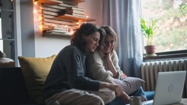 Genç lezbiyen çift kış tatilinde bilgisayar ve akıllı telefon kullanarak online alışveriş yapıyor. 