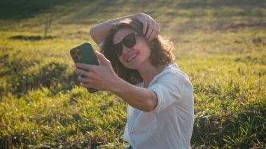 Güneş gözlüğü takan beyaz bir kadın akıllı telefonuyla selfie çekiyor..