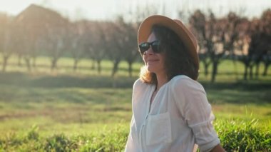 Beyaz şapkalı genç bir kadın çimenlerde otururken temiz havanın ve güneşin tadını çıkarıyor..