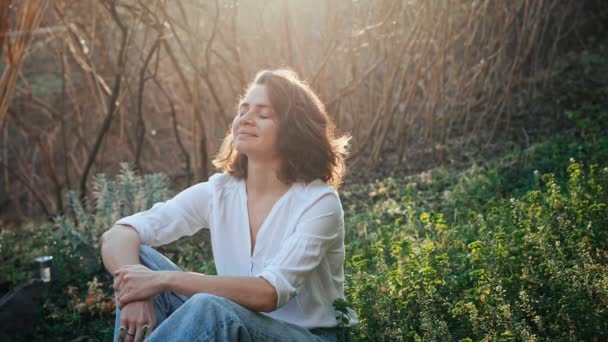 芝生の上に座りながら新鮮な空気と太陽を楽しむ若い白人女性 — ストック動画