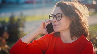 Portrait of a young caucasian cheerful woman talking on the phone while sitting on a bench in the street