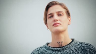 Portrait of a serious and confident caucasian woman. A queer person with short hair looking at the camera.