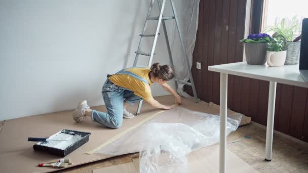 Young Caucasian Woman Preparing Room Painting Female Fixing Film Masking — Stockvideo