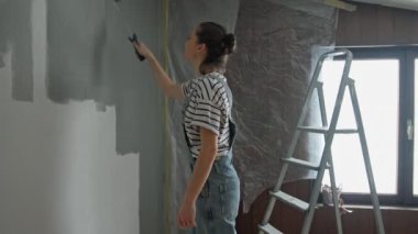 A slow-motion shot of a young woman painting the wall with a roller.