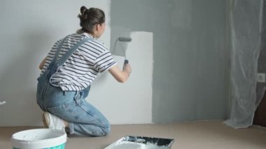 A slow-motion shot of a young woman painting the wall with a roller.
