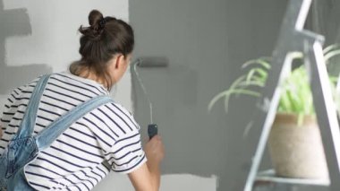 A slow-motion shot of a young woman painting the wall with a roller.