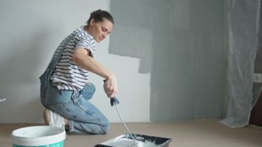A slow-motion shot of a young woman painting the wall with a roller.