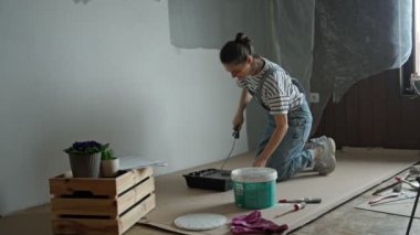 A slow-motion shot of a young woman painting the wall with a roller.