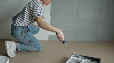 A slow-motion shot of a young woman painting the wall with a roller.