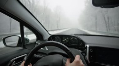 Cinematic footage from the inside of a car. A person driving a car down the winter road.