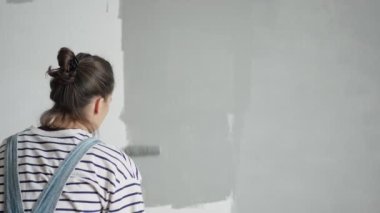A slow-motion shot of a young woman painting the wall with a roller.
