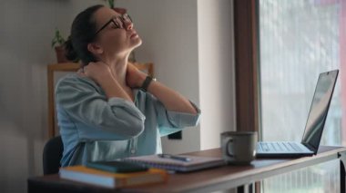 Tired young business woman massaging her neck and taking a break from working on laptop at the home office.