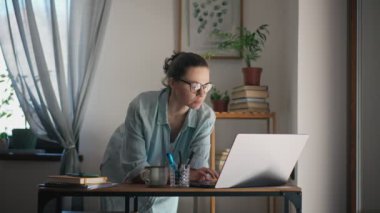 A young adult caucasian serious woman using a laptop while working at her home office.