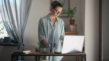 A young adult caucasian serious woman using a laptop while working at her home office.
