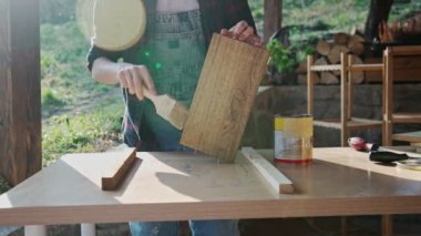 Close-up slow motion footage of a person using a brush to varnish a wooden board.