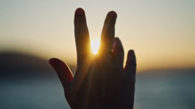 Gün batımında bir insanın elinin yakın çekim görüntüsü güneş ışınlarını yakalar..