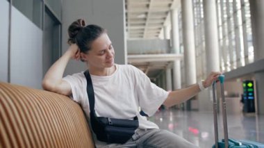 Elinde telefon olan genç bir bayan gezgin havaalanı bekleme salonunda bir bankta oturuyor.