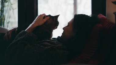 Genç bir kadın, bir kış günü sevimli bir kediyle pencerenin kenarında yatıyor.