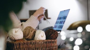İnternette örgü örmeyi öğrenen bir kadının yakın çekimi. Sıcak bir kış akşamında kanepede örgü malzemeleri ve dizüstü bilgisayar.