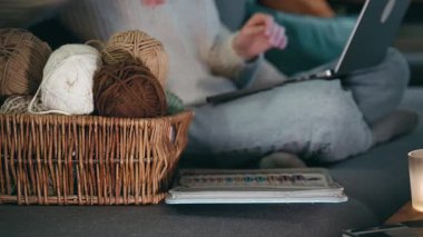 İnternette örgü örmeyi öğrenen bir kadının yakın çekimi. Sıcak bir kış akşamında kanepede örgü malzemeleri ve dizüstü bilgisayar.