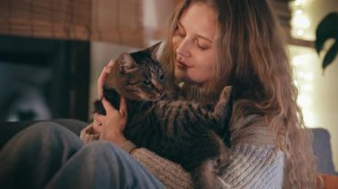 Genç bir kadının akşamları rahat evinde kedisine sarılmasının yakın çekimi.