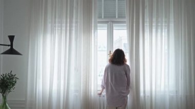 Genç bir kadın pencerede duruyor ve manzaranın tadını çıkarıyor.