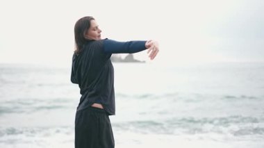 Yağmurda kumsalda dans eden orta yaşlı bir kadının el kamerası görüntüsü.