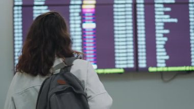 Havaalanının kalkış panosunda duran genç bir kadın yolcu.