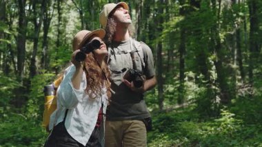 Genç bir çift yürüyüşçü yaz ormanlarında yürürken dürbün kullanıyor.