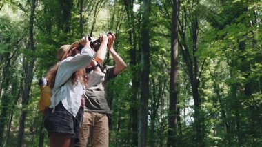 Genç bir çift yürüyüşçü yaz ormanlarında yürürken dürbün kullanıyor.