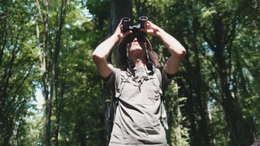 Yaz ormanlarında yürürken dürbün kullanan bir turist.