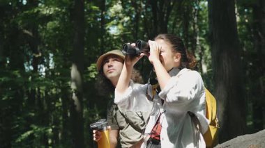 Genç bir çift yürüyüşçü yaz ormanlarında yürürken dürbün kullanıyor.