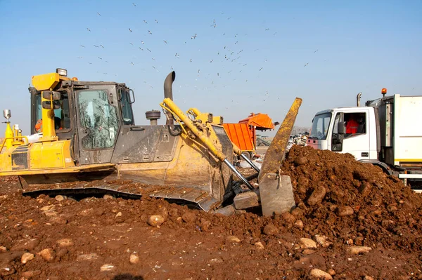 Municipal waste landfill. Workers with trucks and bulldozers at work in waste storage landfill.