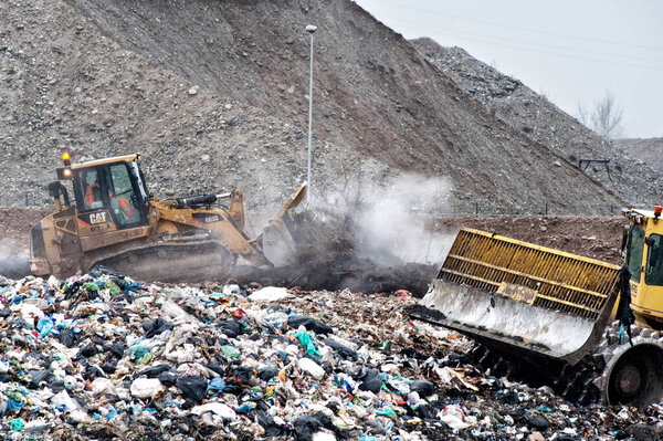 Dump municipal waste. Workers with trucks and bulldozers at work in waste storage landfill.