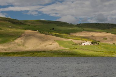 Alta Murgia, parkın manzarası çayır, mavi gökyüzü ve bulutlar, göl ve çiftlik evleri. İtalya 'nın Puglia kentindeki yeşil tepelerin arasındaki göl..