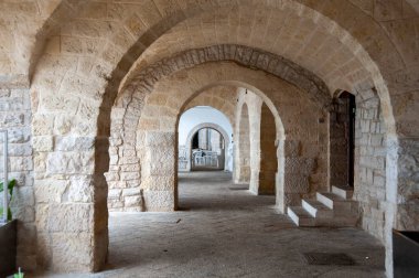 Büyük kaba bloklardan yapılmış bir dizi yarı dairesel kemer içeren taş koridor. Kemerler derinlik ve perspektif duygusu yaratır. Gözü uzak bir kapıya götürür..
