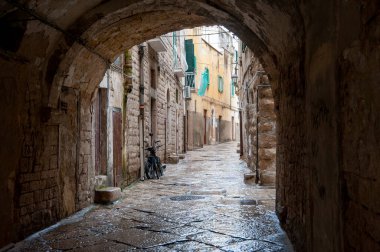 İtalya 'nın güneyindeki bir köyde dar bir kaldırıma çıkan taş bir kemer yolu. Kemer yolu eski ve kırsal, görünür grafitileri var. Kireçtaşı binalar yol boyunca uzanıyor. Güney İtalya