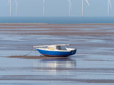 Yelkenli, alçak gelgitte karaya oturmuş, rüzgar türbinleri uzakta.