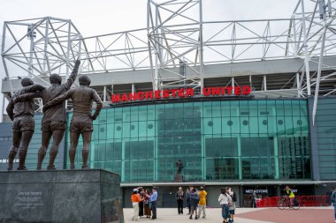 Manchester Trafford UK 29 Haziran 2024. Turistler bulutlu bir günde ünlü futbol stadyumunun dışındaki Birleşmiş Üçlü heykelinin etrafında toplandılar..