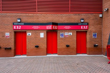 Manchester Trafford UK 29 Haziran 2024. Parlak kırmızı stadyumun giriş kapılarında tuğla bir duvarda E32 etiketi var, East Stand, minimalist şehir tasarımı.