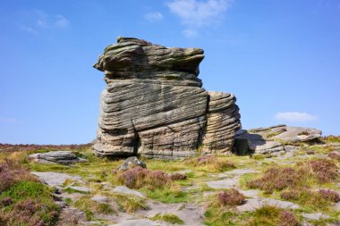 Hathersage Moor Derbyshire UK 'de. Çimenli bir arazide, açık mavi gökyüzünün altında büyük bir kaya oluşumu..