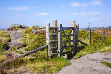 Hathersage moor Derbyshire UK. A rustic wooden gate with a latch amidst a scenic countryside landscape on a sunny day. clipart