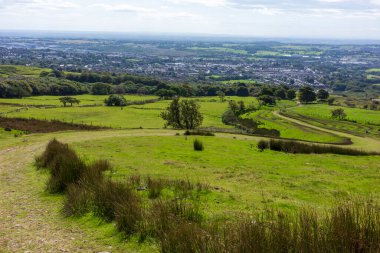 Rolling green hills overlooking Horwich a distant town under a cloudy sky. clipart