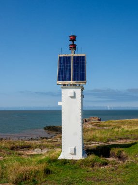 Solar-powered lighthouse standing tall by the sea under a clear blue sky. Hilbre Island. clipart