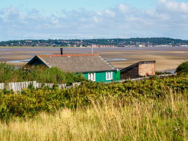 Batı Kirby, Hoylake, İngiltere. 28 Eylül 2024: engin, kumlu haliçlere bakan yeşil ahşap kulübe parlak, mavi bir gökyüzünün altında.